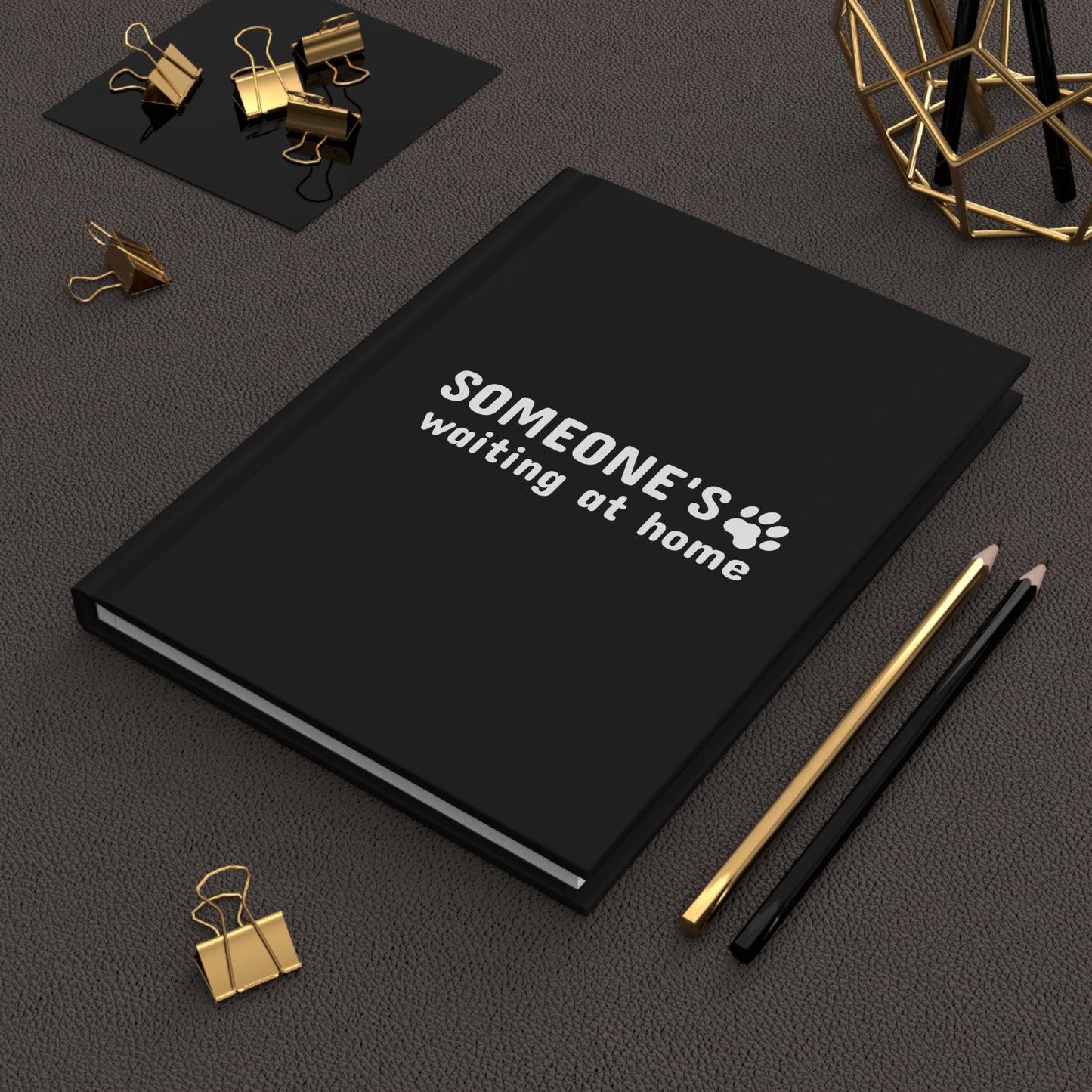 Black notebook with text and paw print design on a dark surface with office supplies.