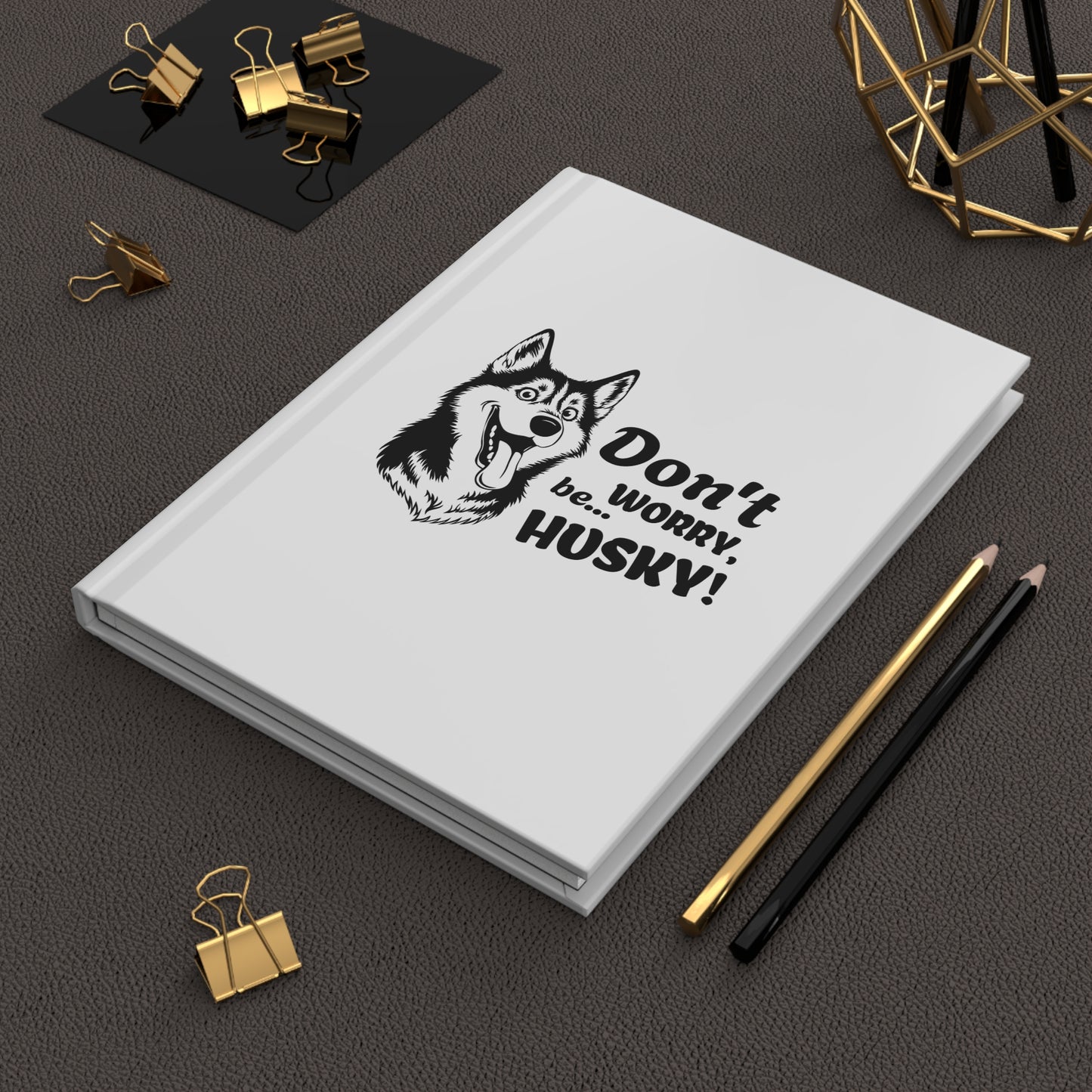 White notebook with husky illustration and text on a dark surface with office supplies.