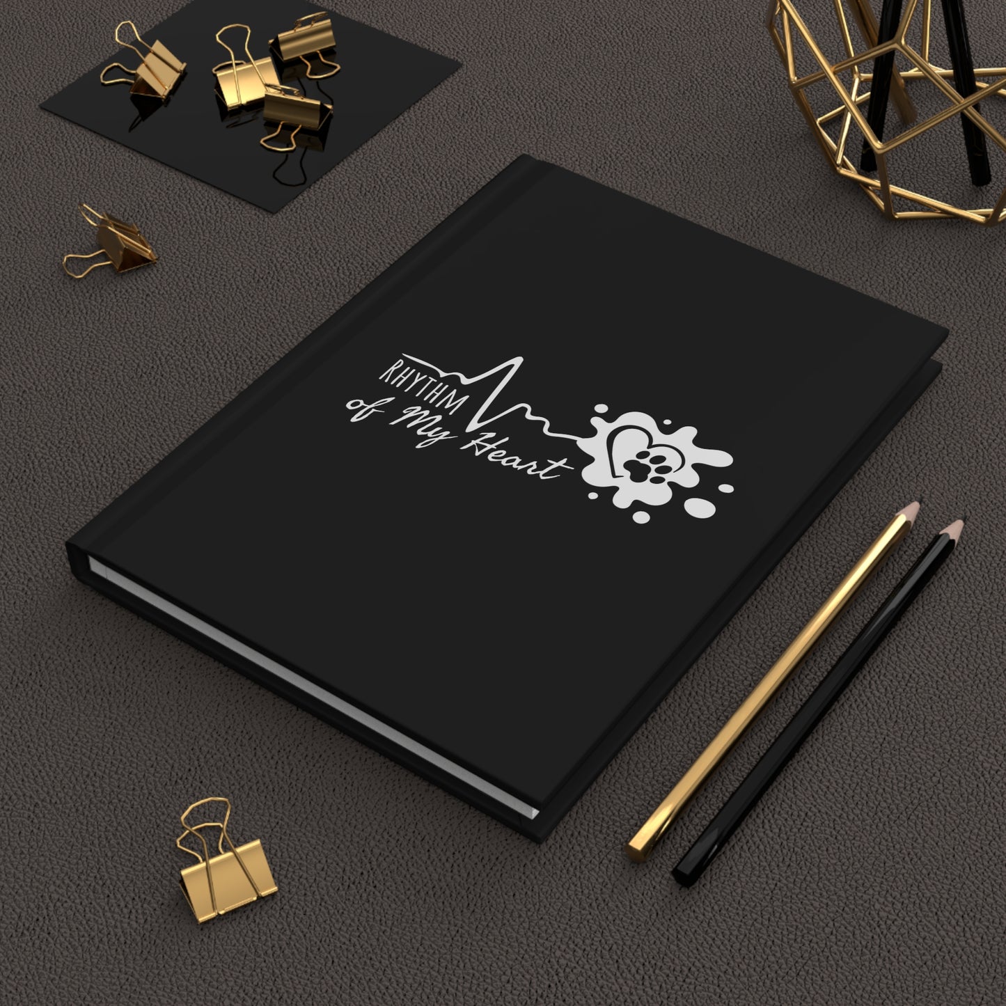 Black notebook with 'Rhythm of My Heart' design on a dark surface with office supplies.