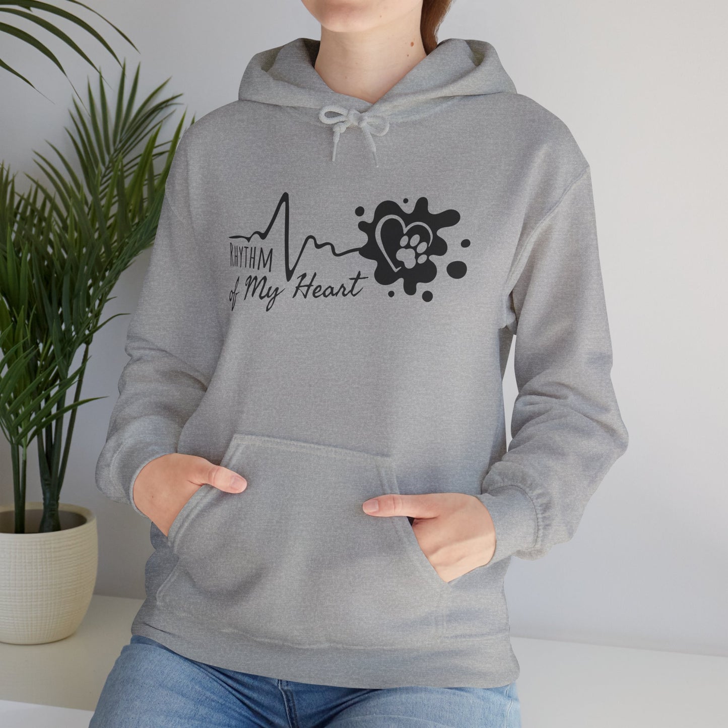 Person wearing a gray hoodie with a heart-themed design in a room with a plant.