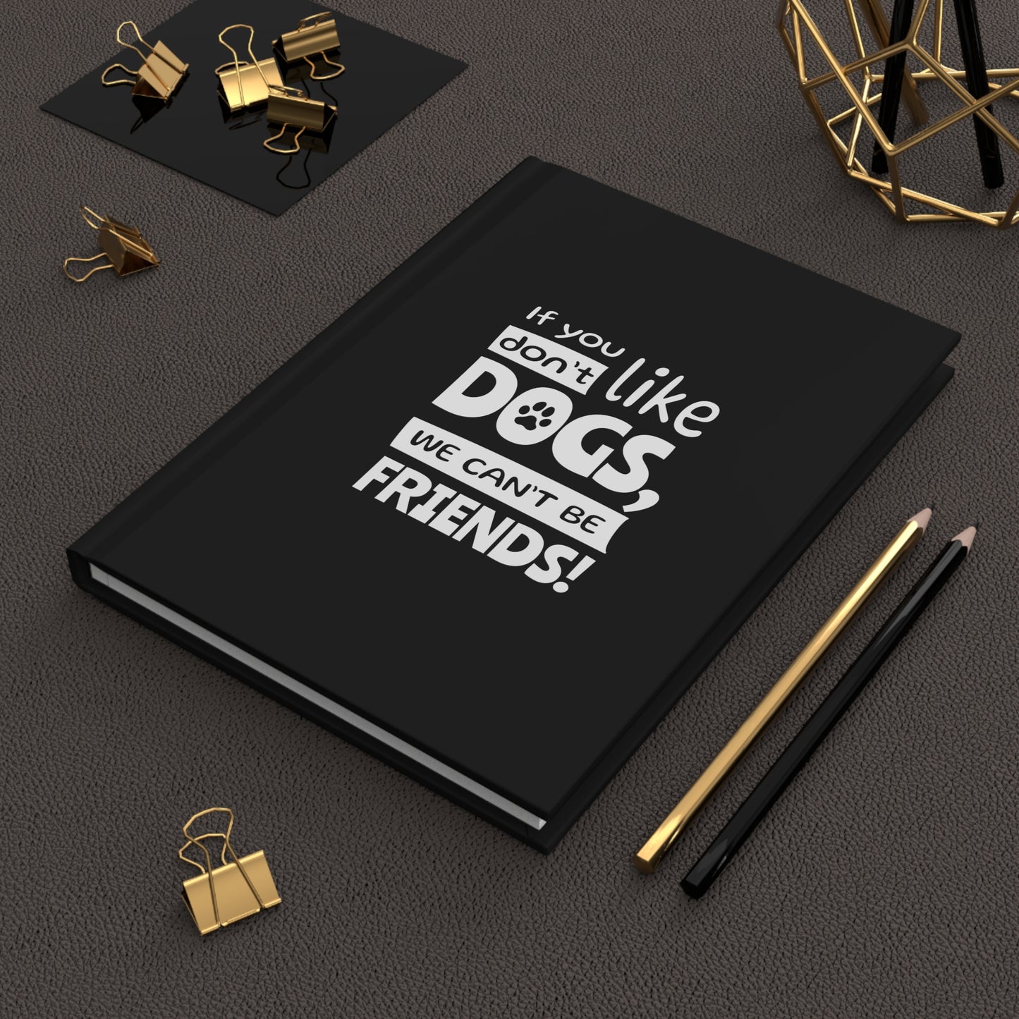 Black notebook with 'If you don't like dogs, we can't be friends!' text on a dark surface with office supplies.