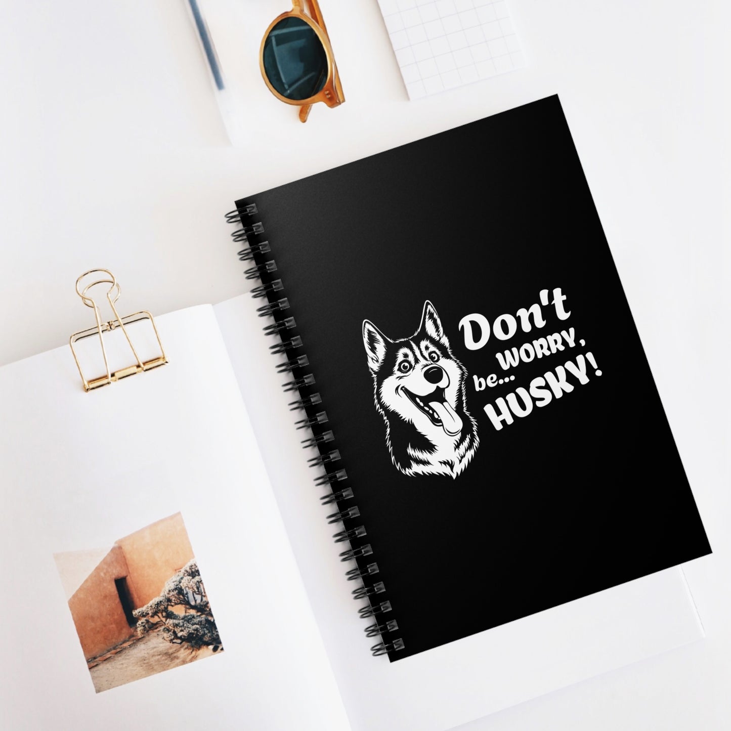 Black notebook with husky illustration and text on a white surface with photos and sunglasses.