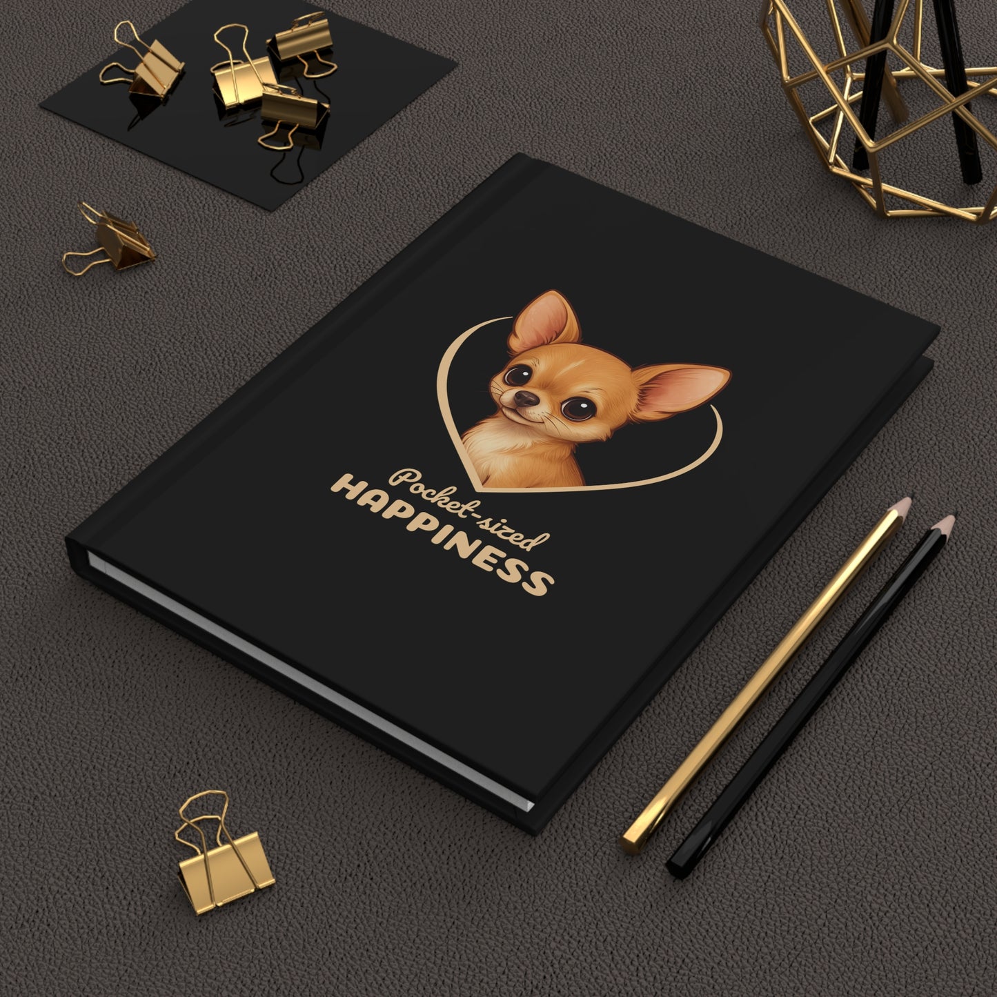 Black notebook with a dog illustration and 'Pocket-sized Happiness' text on a dark surface with office supplies.