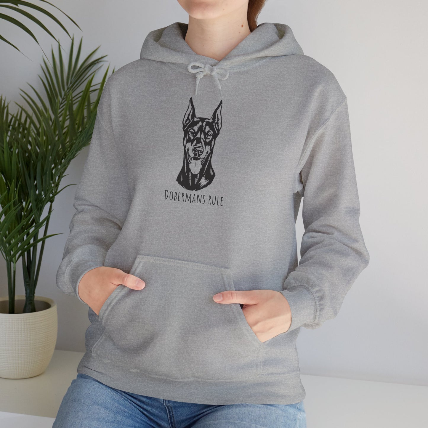 Person wearing a gray hoodie with a dog illustration and 'Dobermans Rule' text, standing indoors.
