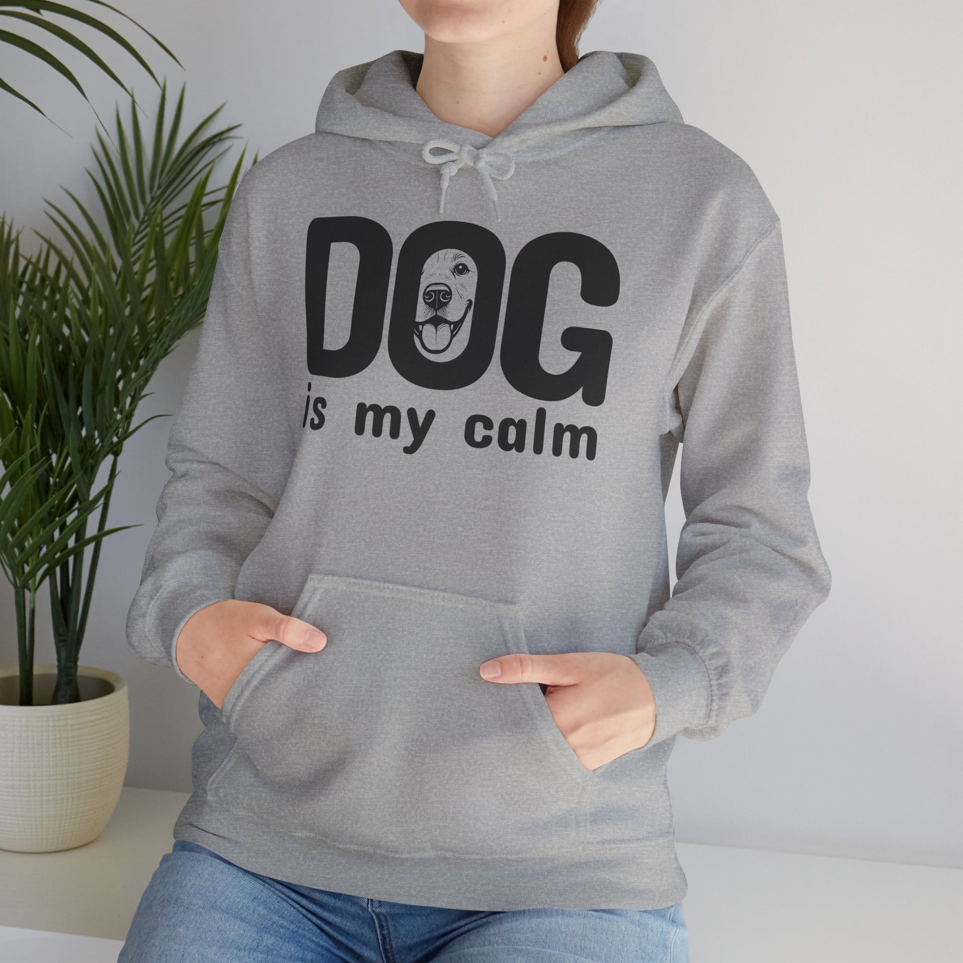 Person wearing a gray hoodie with 'DOG is my calm' text, standing indoors with a plant in the background.