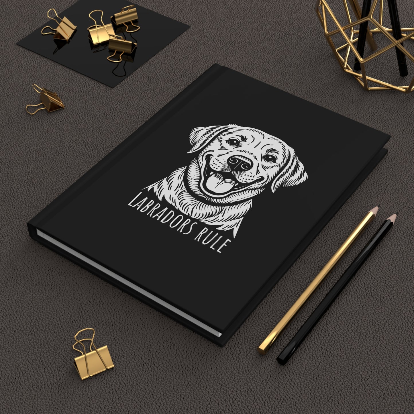 Black notebook with a dog illustration and 'Labradors Rule' text on a dark surface with office supplies.
