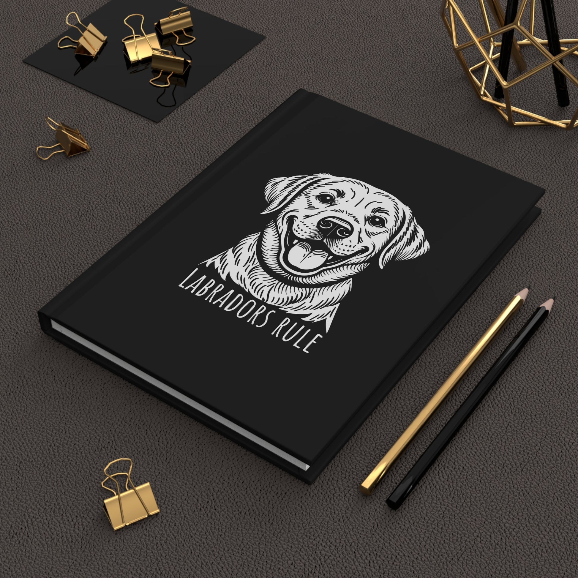 Black notebook with a dog illustration and 'Labradors Rule' text on a dark surface with office supplies.
