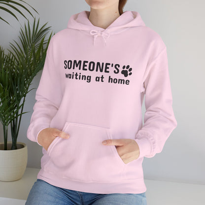Person wearing a pink hoodie with text and paw print design, standing indoors next to a plant.