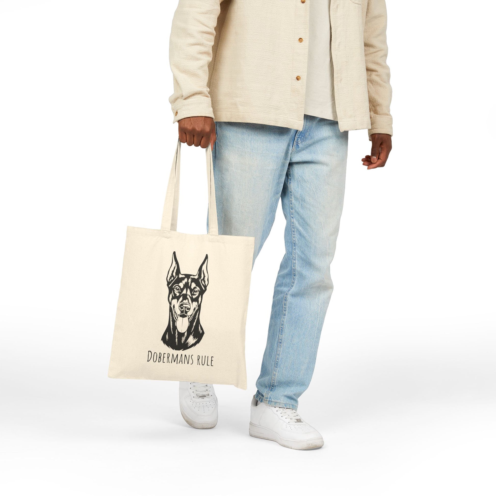 Person holding a tote bag with a dog illustration and 'Dobermans Rule' text on a white background