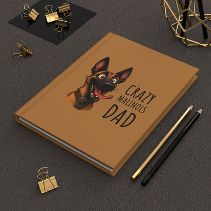 Brown notebook with a dog illustration and text on a dark surface with office supplies.