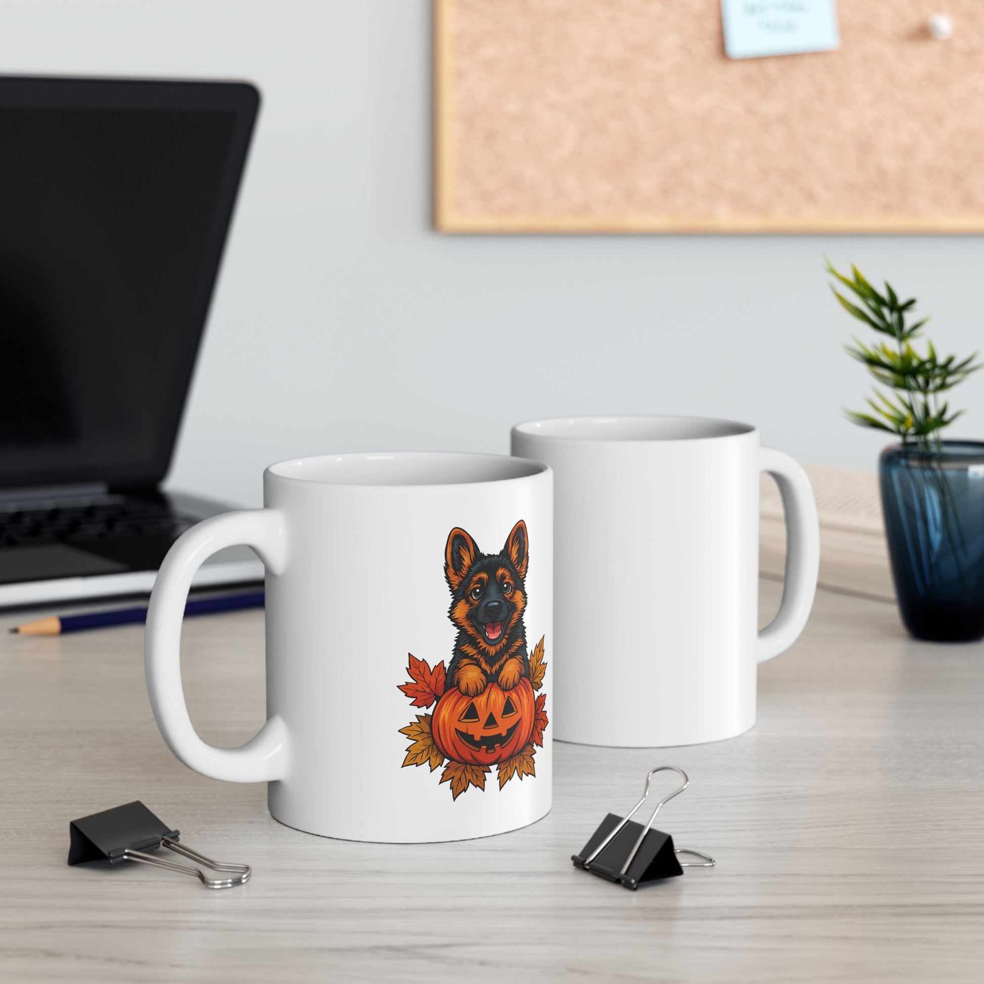 Two white mugs on a desk with one featuring a German Shepherd and pumpkin design.