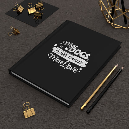 Black notebook with 'More Dogs, More Chaos, More Love' text on a dark surface with office supplies.