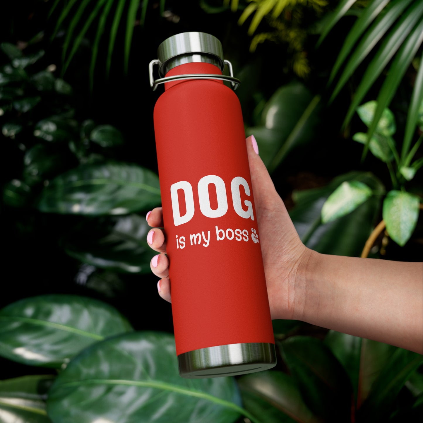 Red water bottle with 'DOG is my boss' text held by a hand against a green leafy background