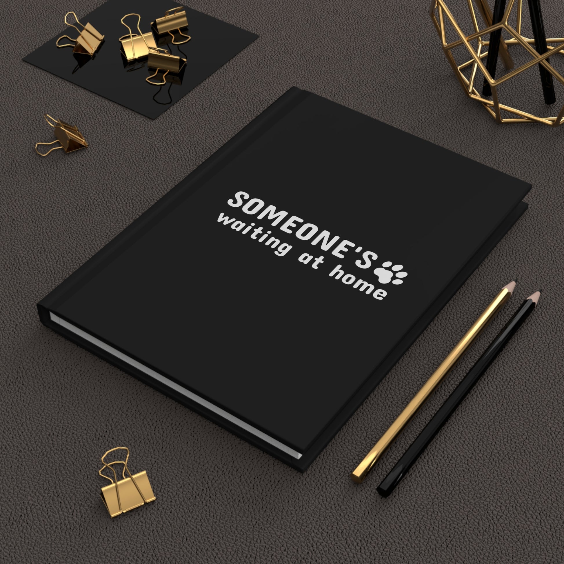 Black notebook with text and paw print design on a dark surface with office supplies.