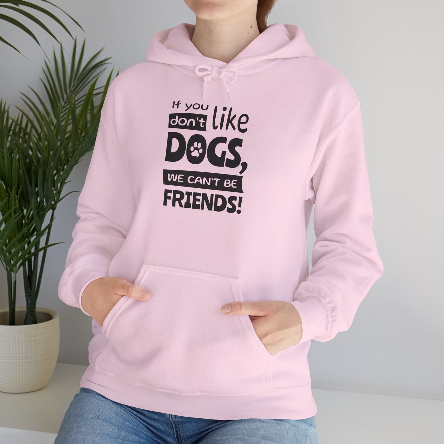 Person wearing a pink hoodie with a humorous text design, standing indoors next to a plant.