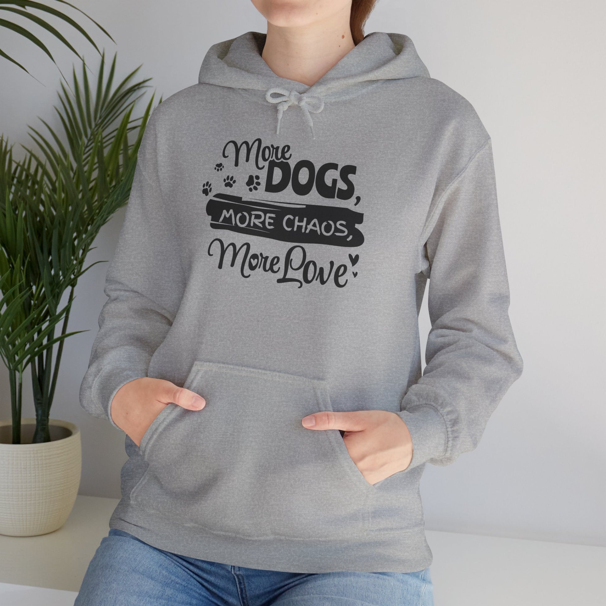 Person wearing a gray hoodie with text 'More Dogs, More Chaos, More Love' in a home setting.