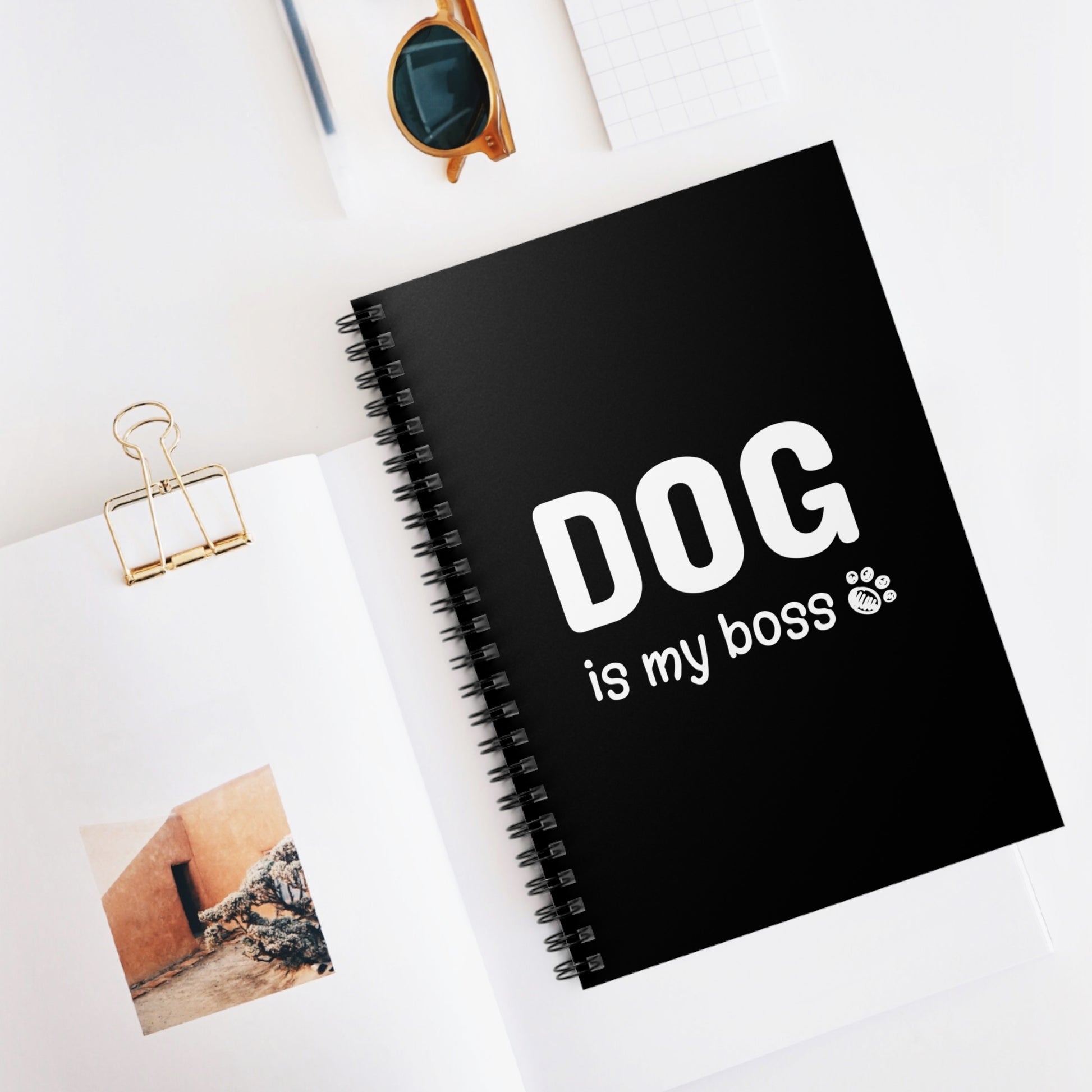 Black notebook with 'DOG is my boss' text on a white surface with sunglasses and photos.