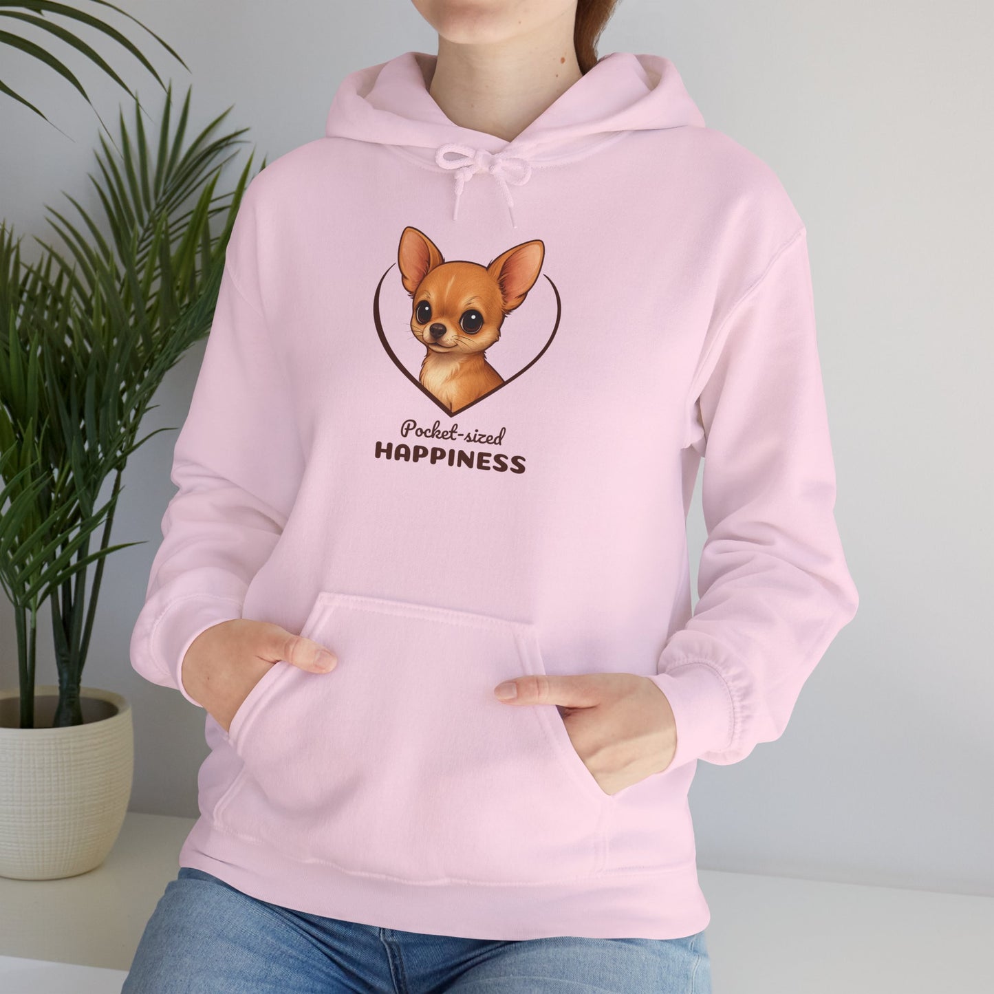 Person wearing a pink hoodie with a dog illustration and text, standing next to a plant.