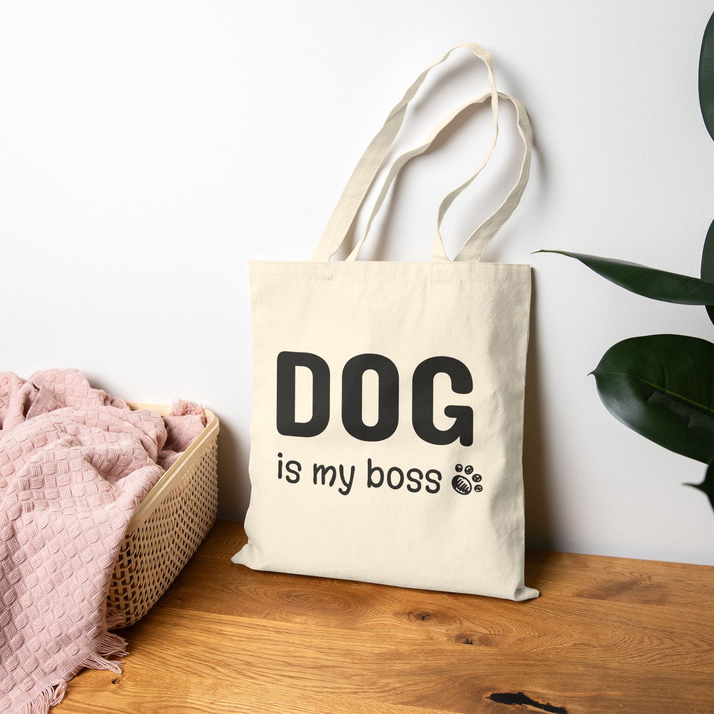 Beige tote bag with 'DOG is my boss' text on a wooden surface with a plant in the background