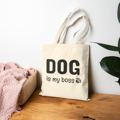 Beige tote bag with 'DOG is my boss' text on a wooden surface with a plant in the background