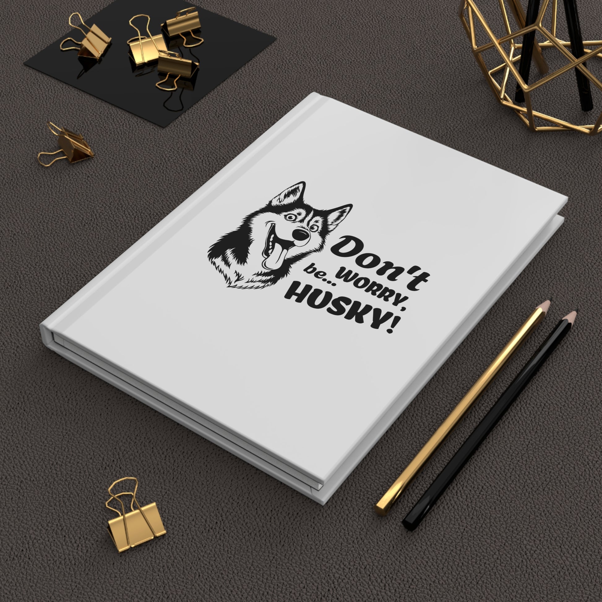 White notebook with husky illustration and text on a dark surface with office supplies.