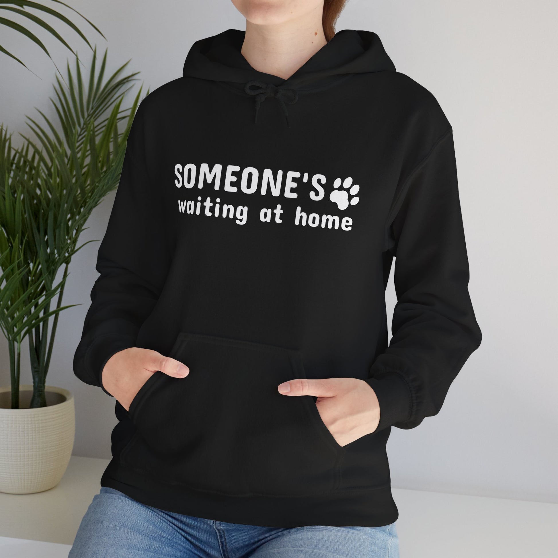 Person wearing a black hoodie with 'SOMEONE'S waiting at home' text and paw print design.