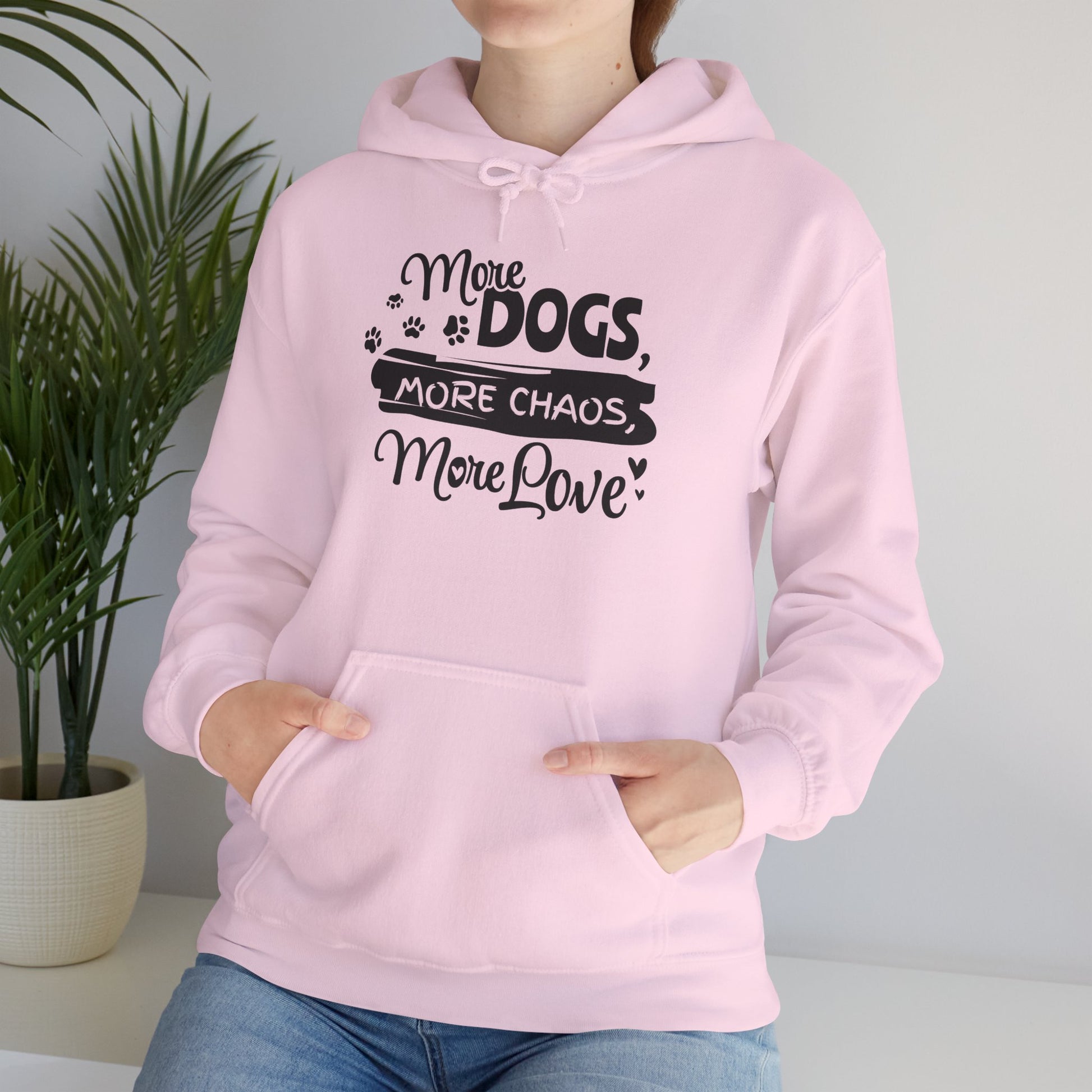 Person wearing a pink hoodie with text 'More dogs, more chaos, more love' in a home setting.