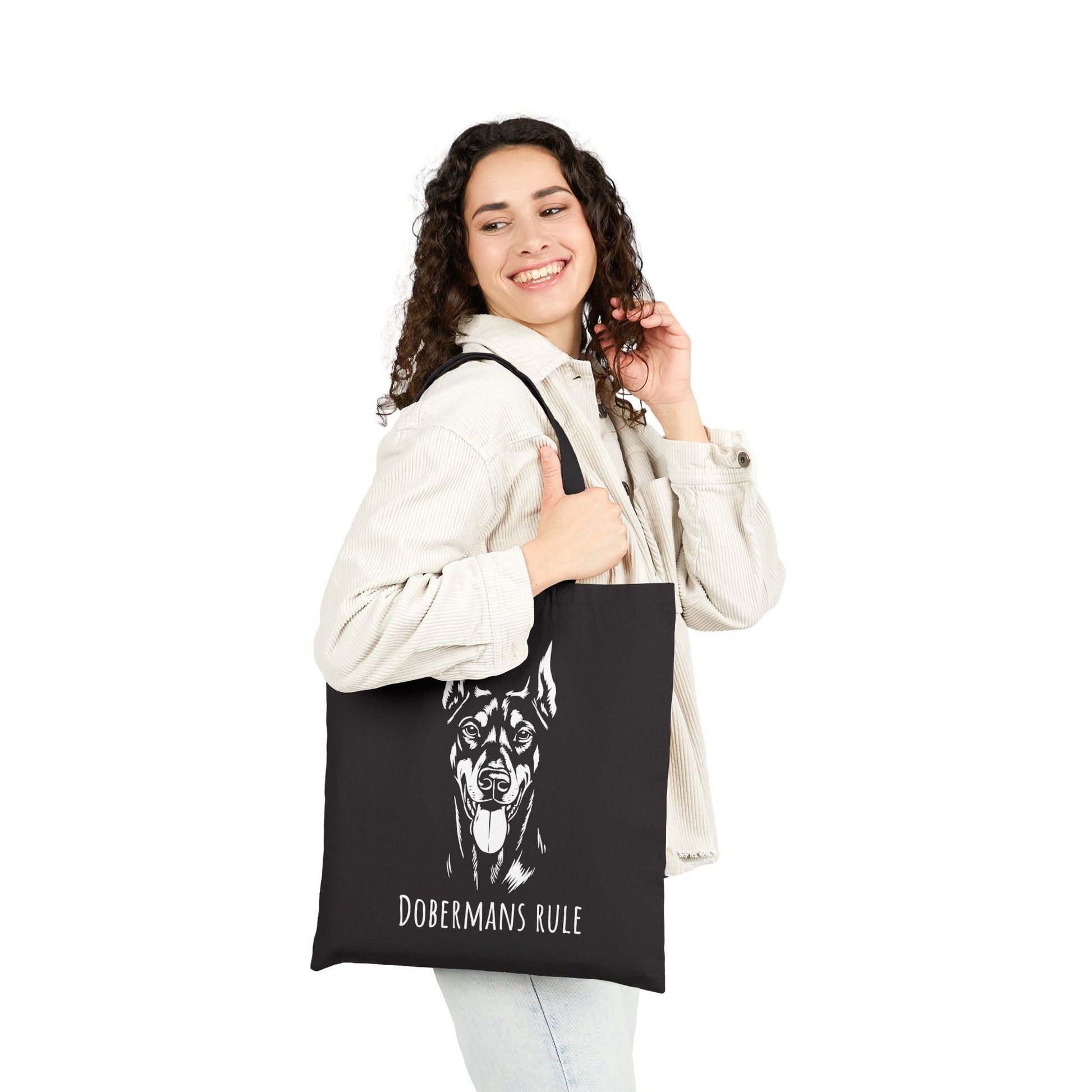 Woman holding a black tote bag with 'Dobermans Rule' text and dog illustration on a white background
