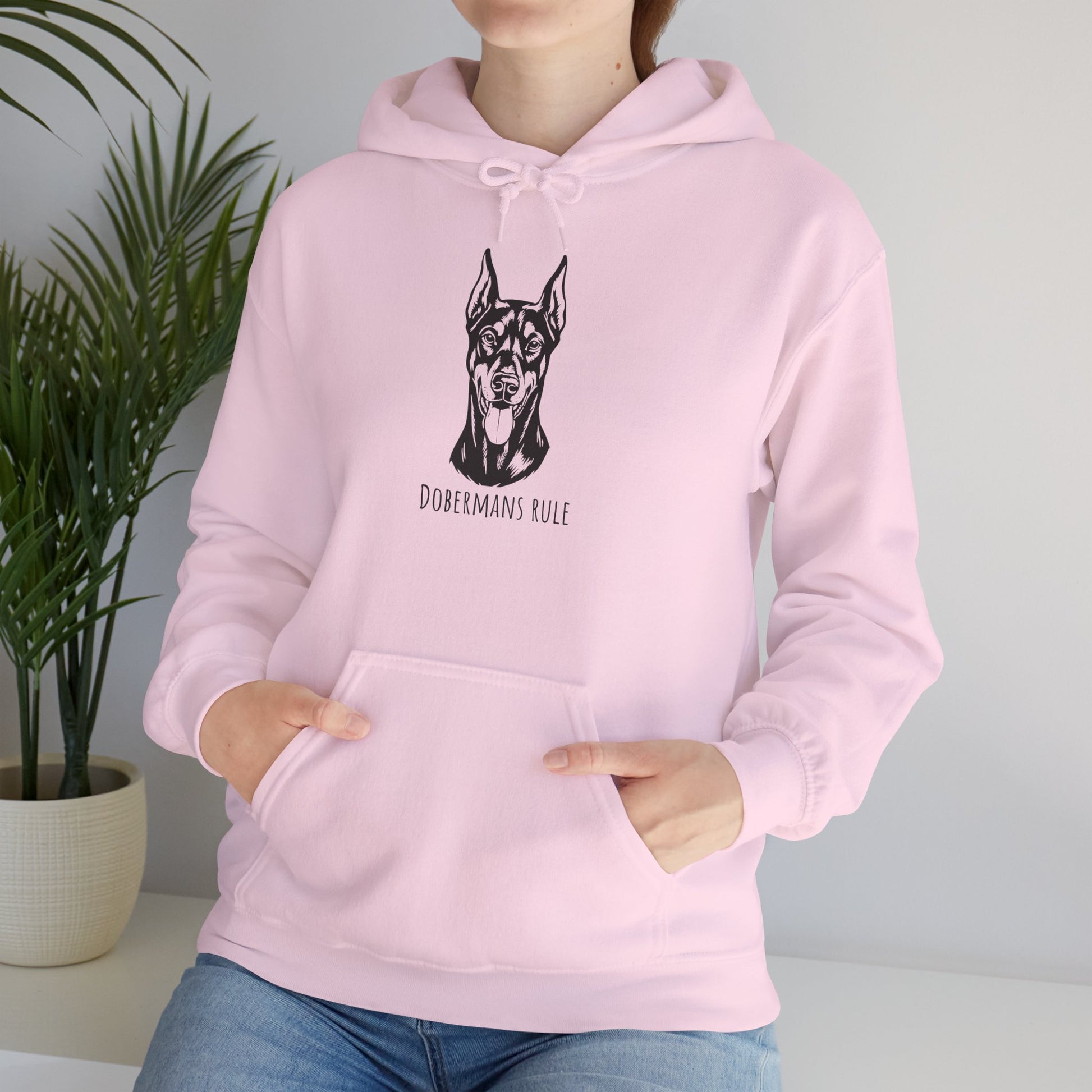 Person wearing a pink hoodie with a dog illustration and 'Dobermans Rule' text, standing next to a plant.
