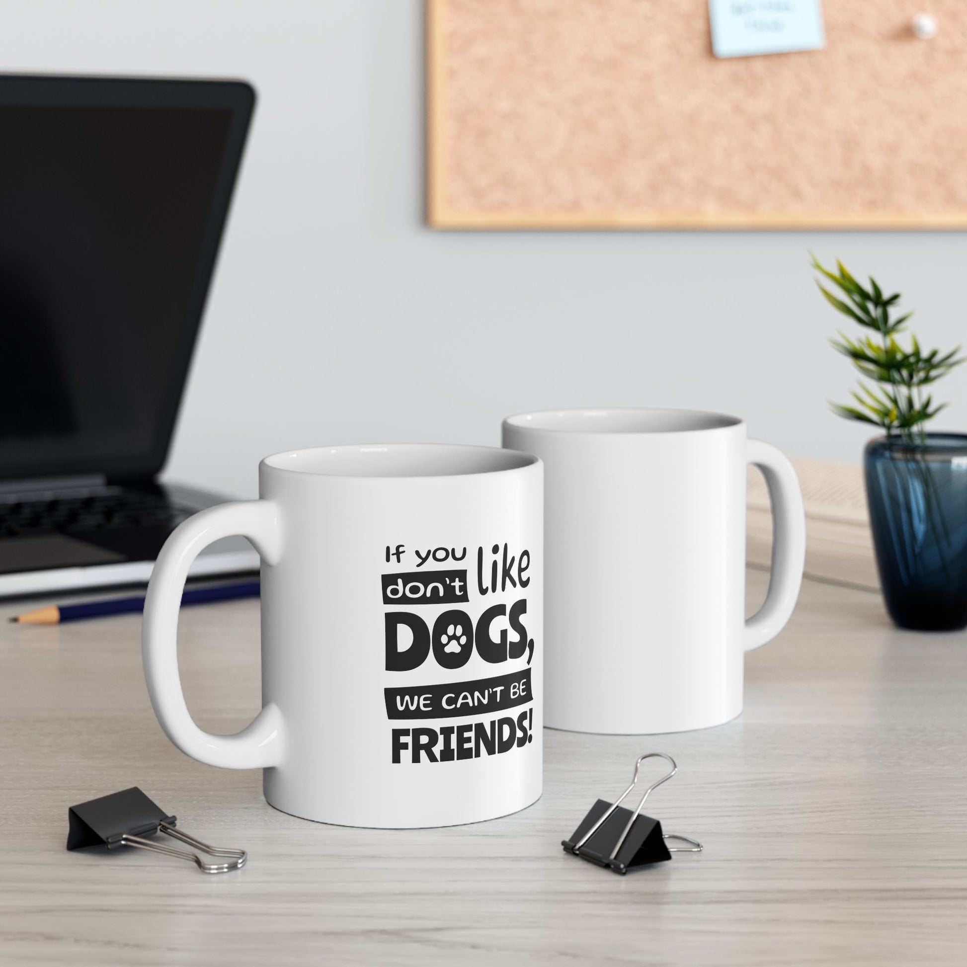 Two white mugs on a desk with one displaying a humorous dog-themed message.