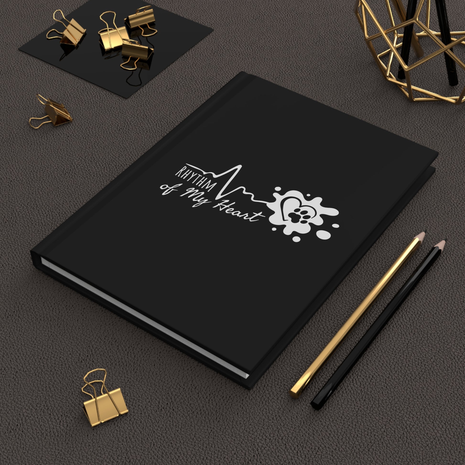 Black notebook with 'Rhythm of My Heart' design on a dark surface with office supplies.