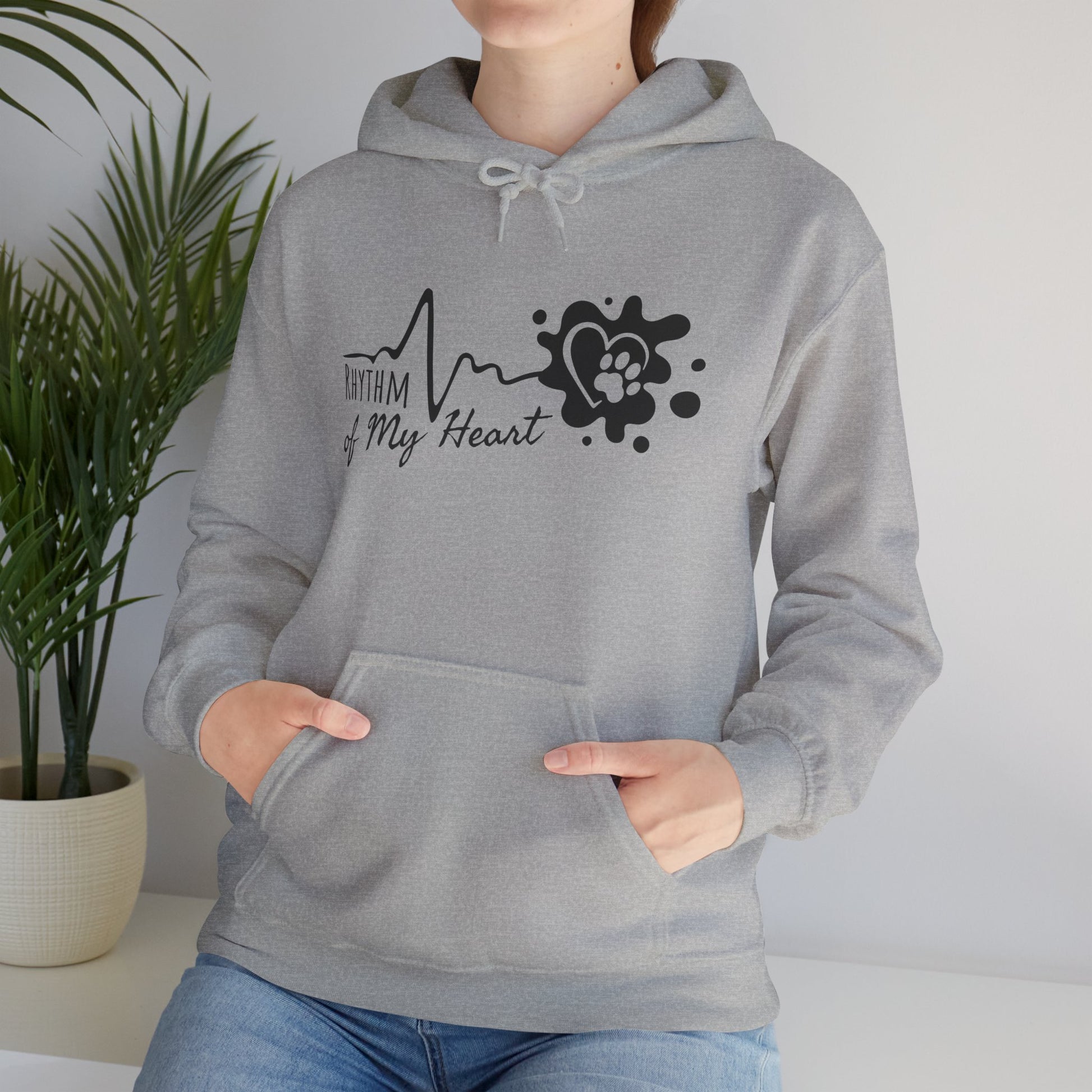 Person wearing a gray hoodie with a heart-themed design in a room with a plant.