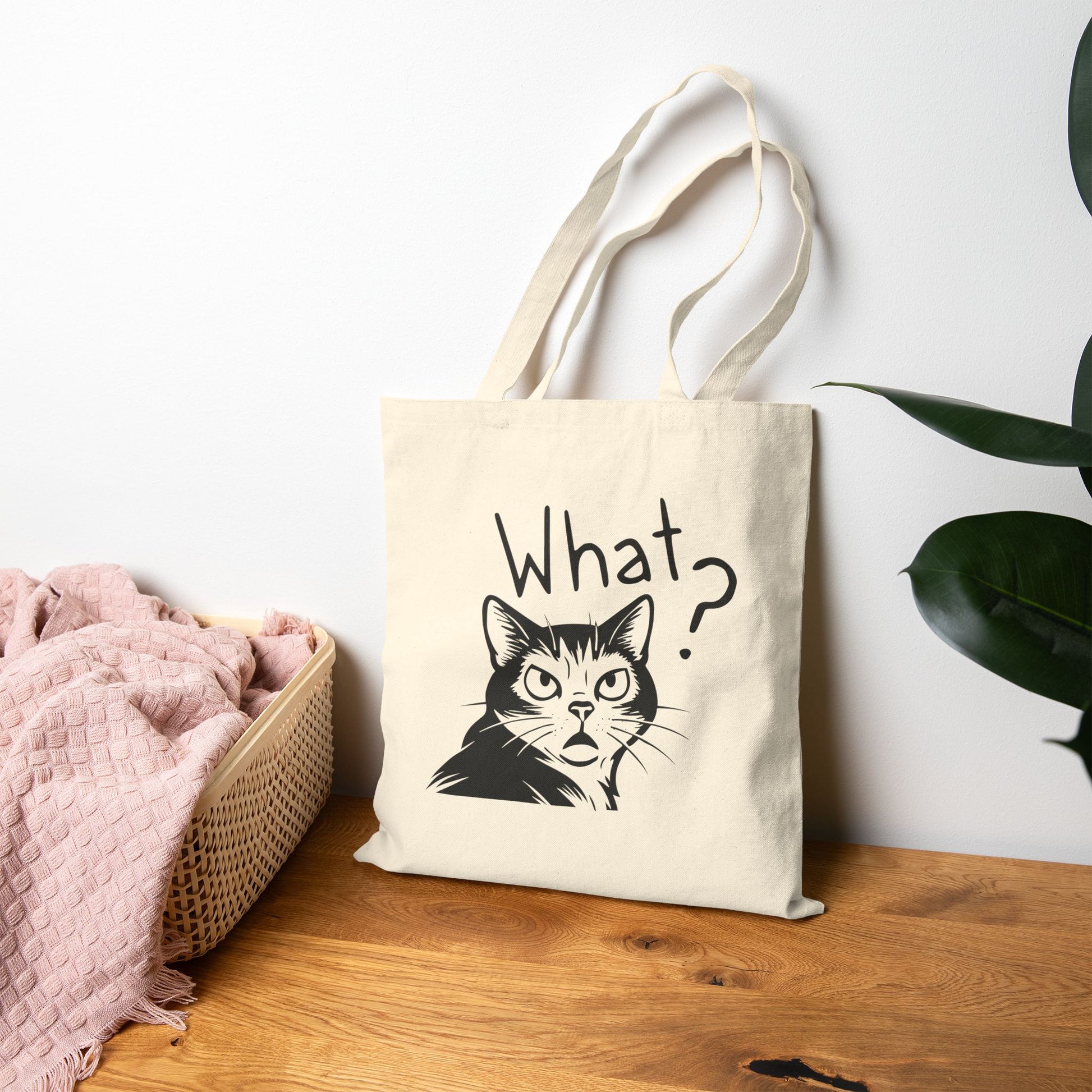 Tote bag with a cat illustration and 'What?' text on a wooden surface.