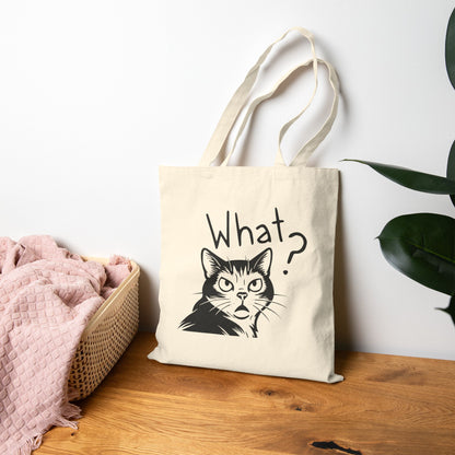 Tote bag with a cat illustration and 'What?' text on a wooden surface.