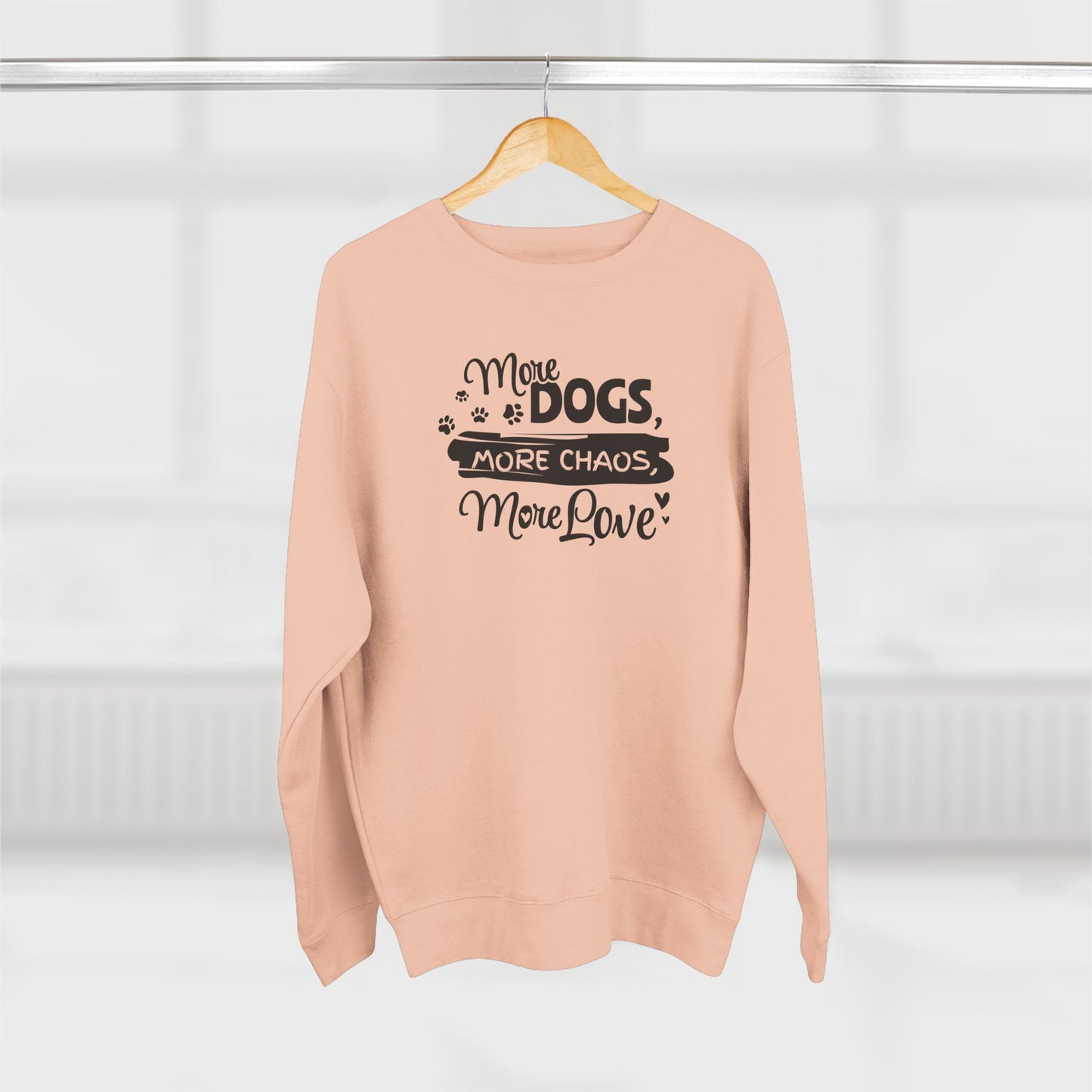 Pink sweatshirt with text 'More Dogs, More Chaos, More Love' on a hanger against a white background