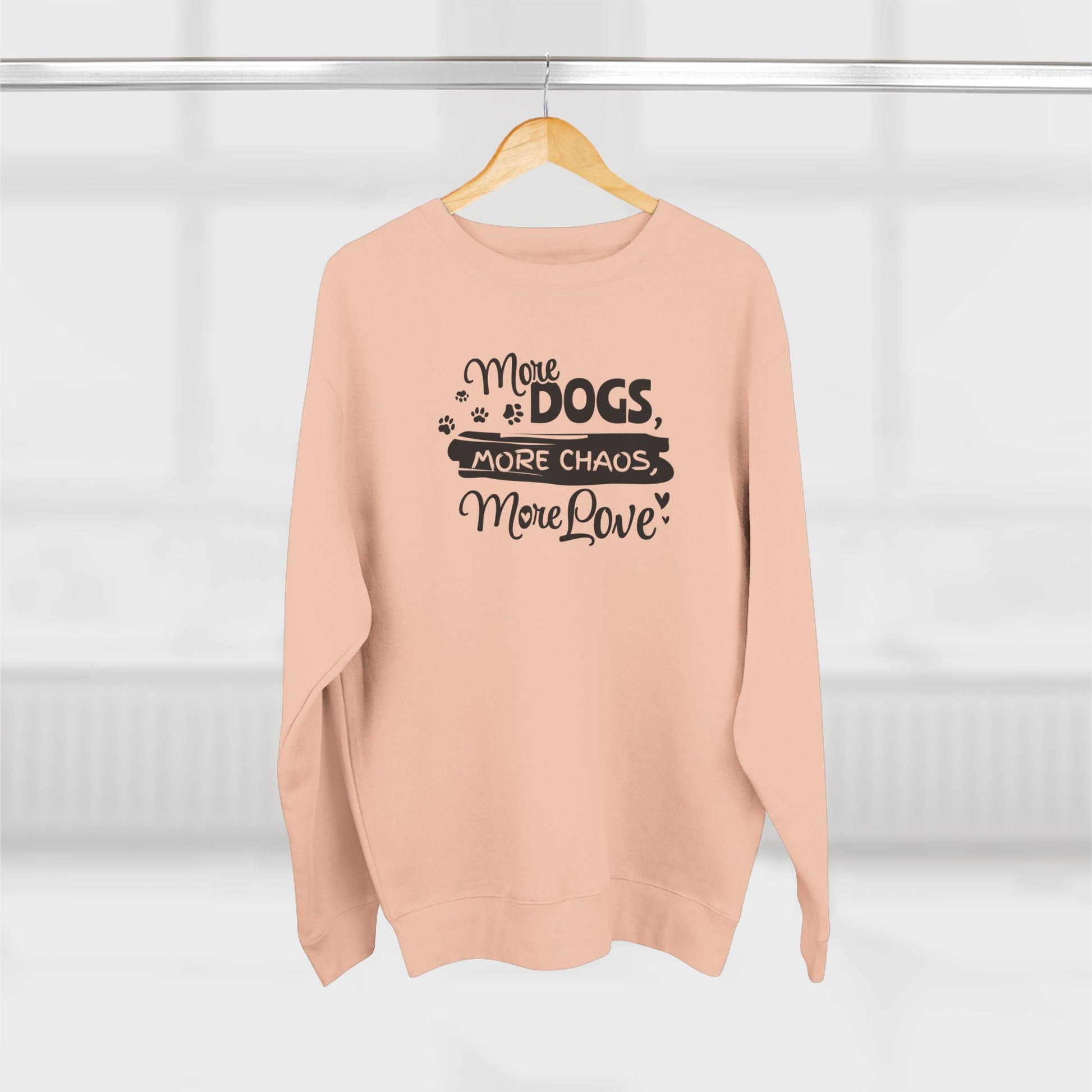Pink sweatshirt with text 'More Dogs, More Chaos, More Love' on a hanger against a white background