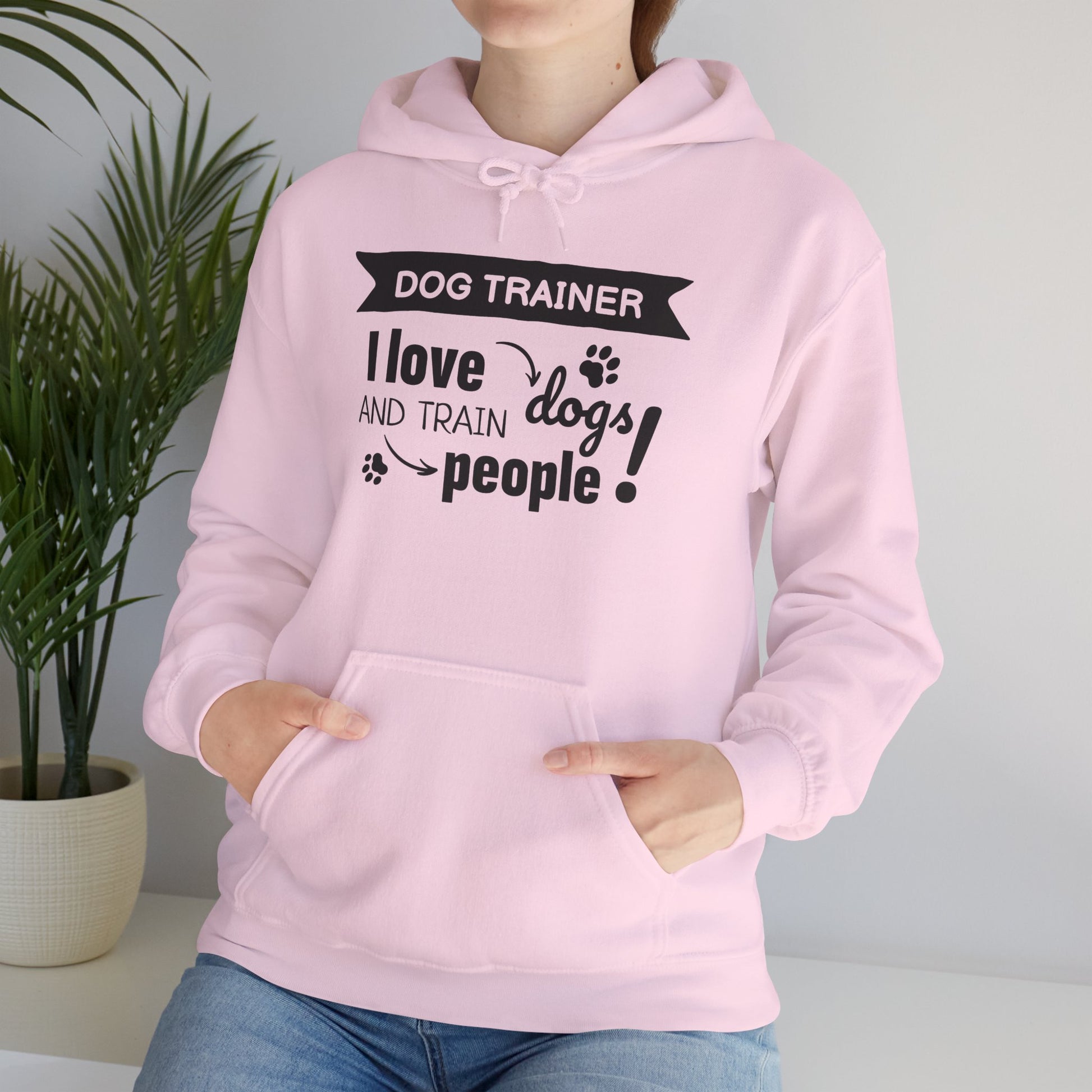 Person wearing a pink hoodie with text design, standing indoors next to a plant.