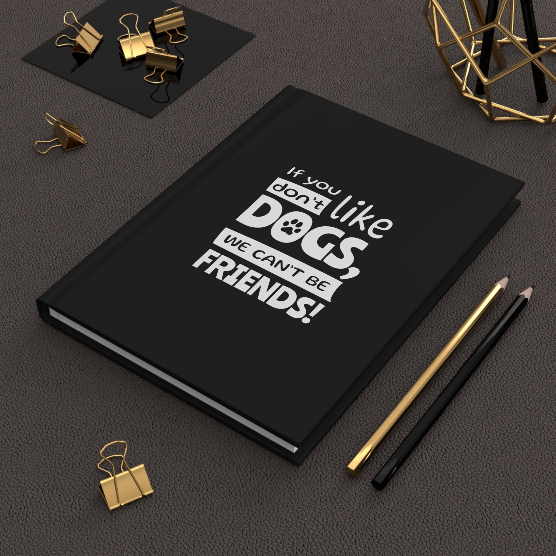 Black notebook with 'If you don't like dogs, we can't be friends!' text on a dark surface with office supplies.