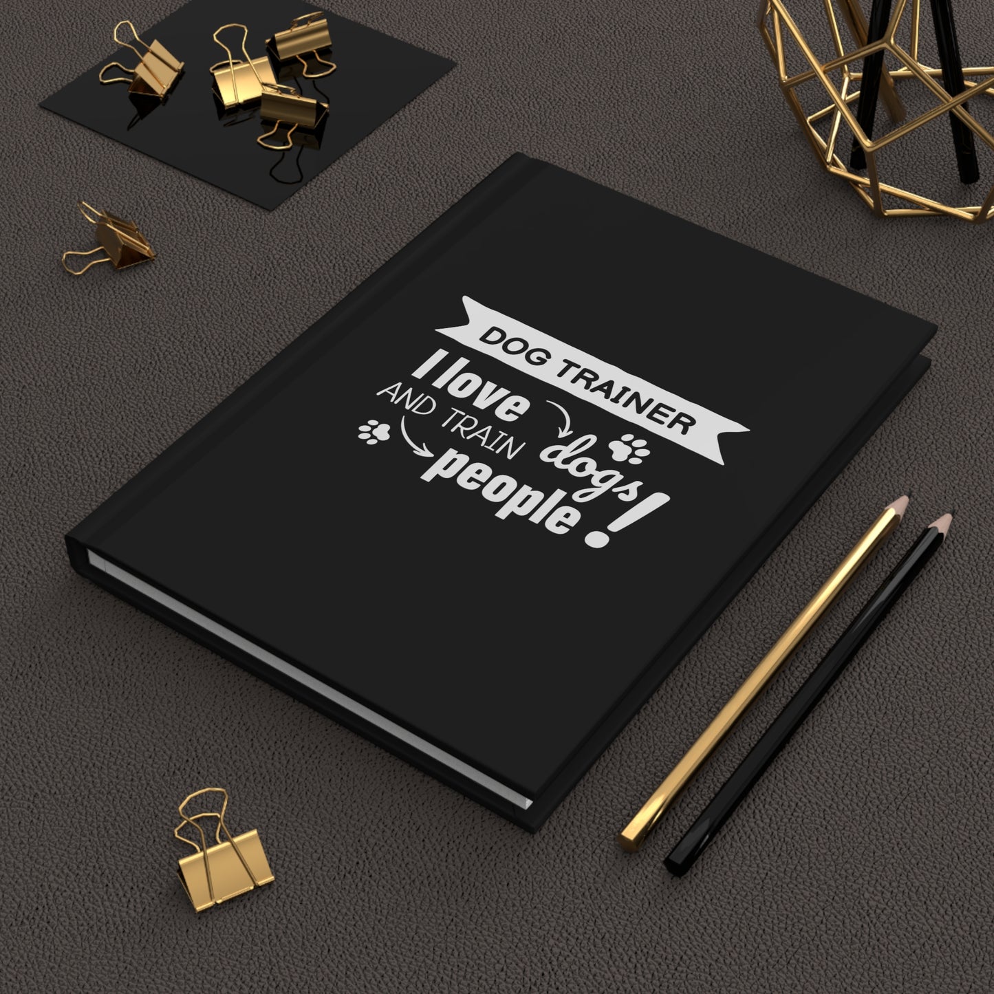 Black notebook with a white text design on a dark surface with office supplies.