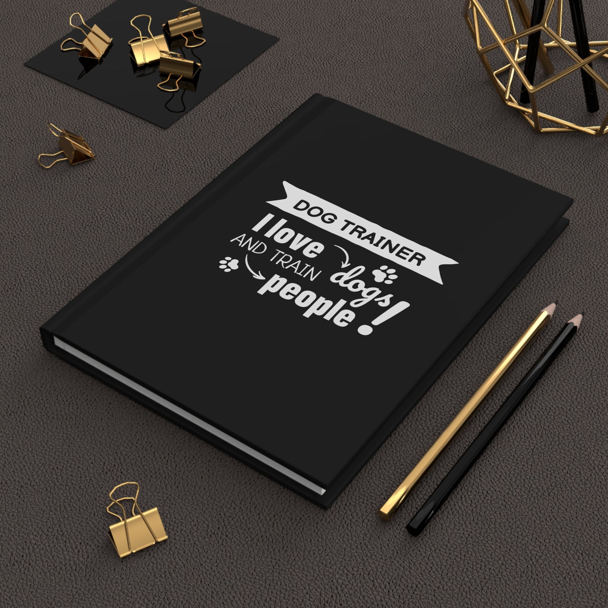 Black notebook with a white text design on a dark surface with office supplies.