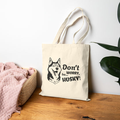 Beige tote bag with husky design and text on a wooden surface with a plant in the background