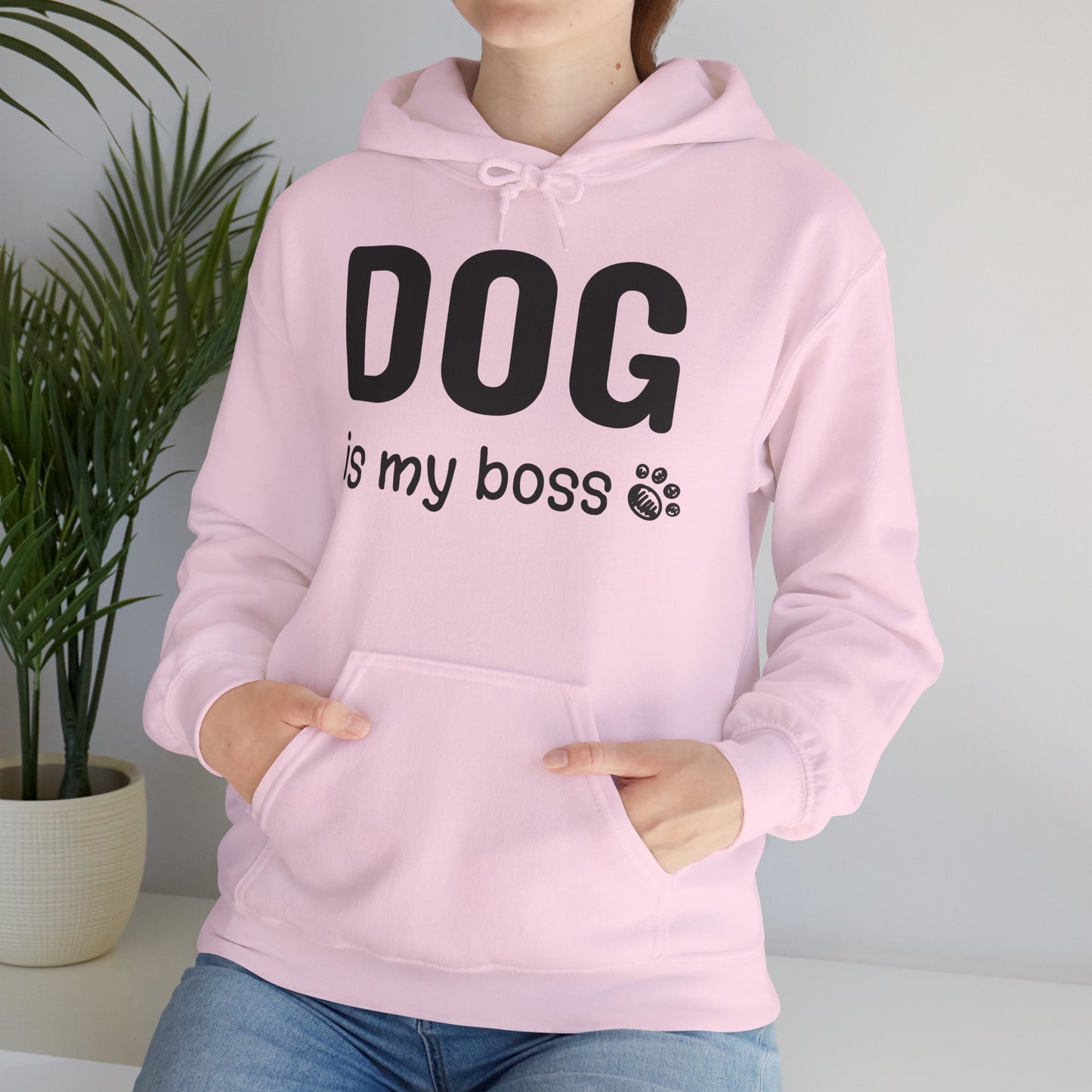 Person wearing a pink hoodie with 'DOG is my boss' text, standing indoors next to a plant.