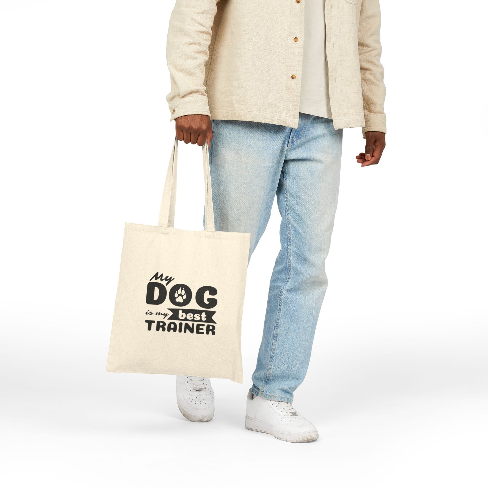 Person holding a tote bag with 'My dog is my best trainer' text on a white background