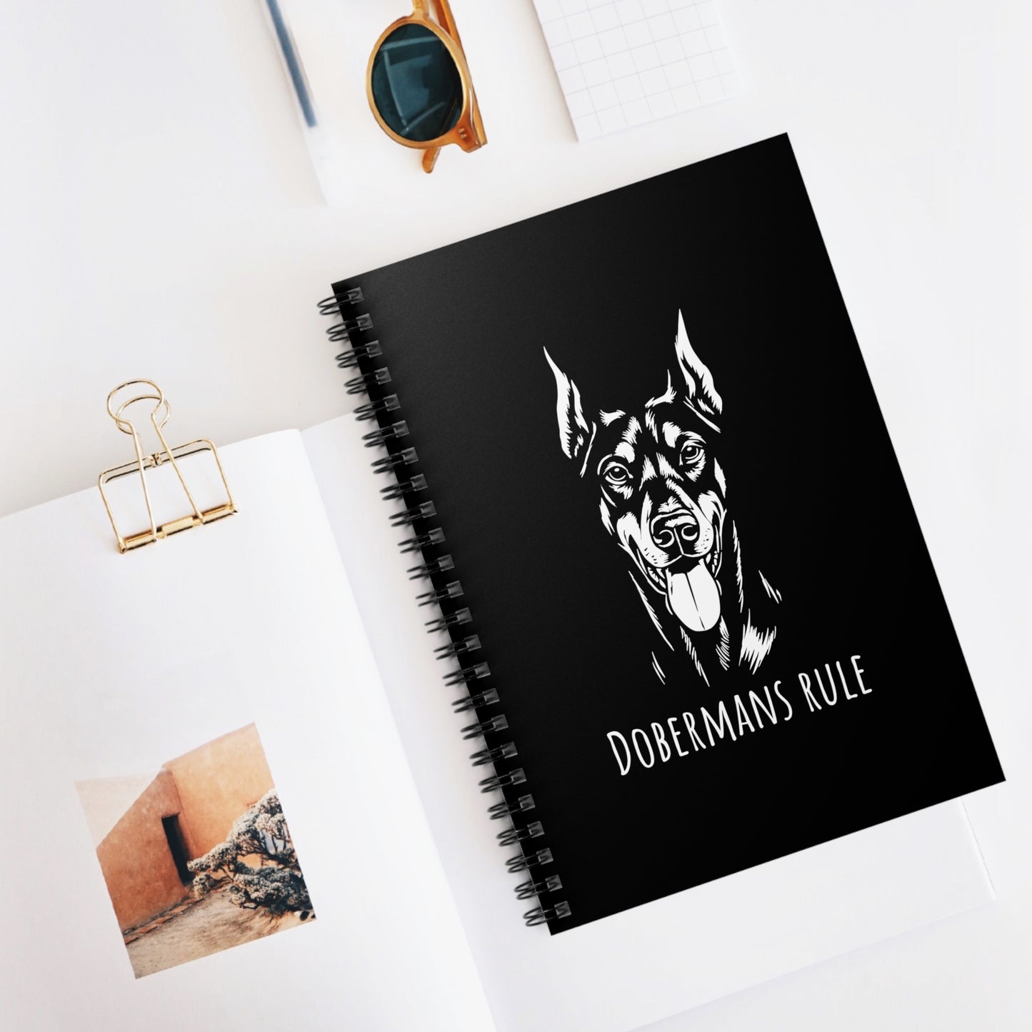 Black notebook with a Doberman illustration and 'Dobermans Rule' text on a white surface.