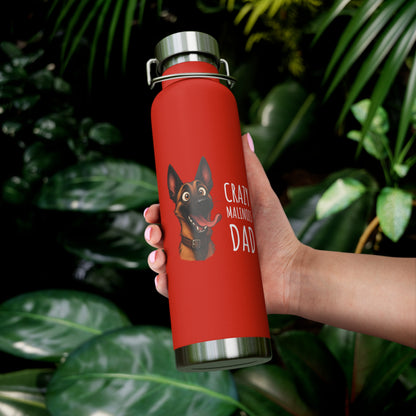Red water bottle with a dog illustration and text held by a hand against a leafy background
