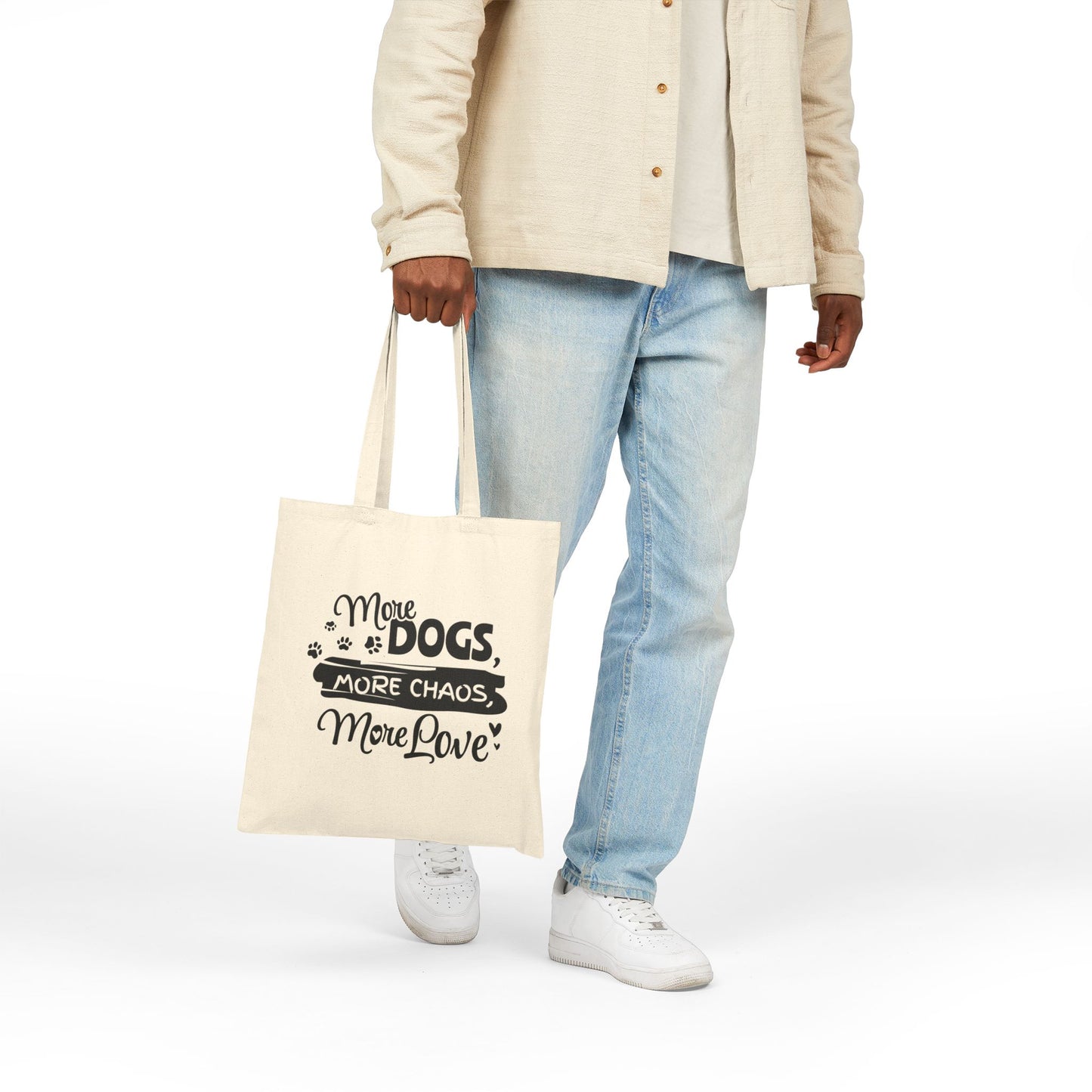 Person holding a tote bag with text 'More dogs, more chaos, more love' on a white background