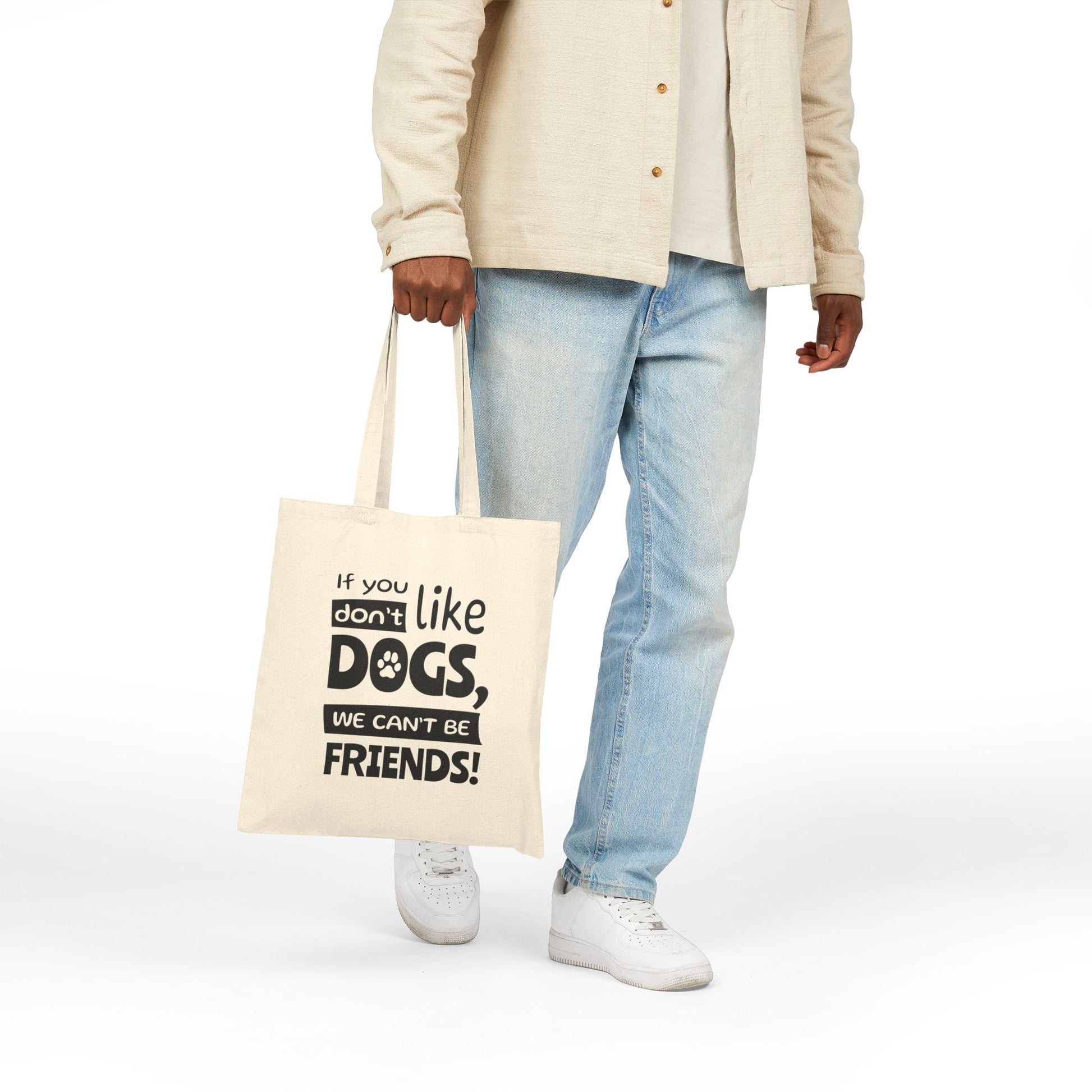 Person holding a tote bag with text, wearing a beige jacket and light blue jeans on a white background