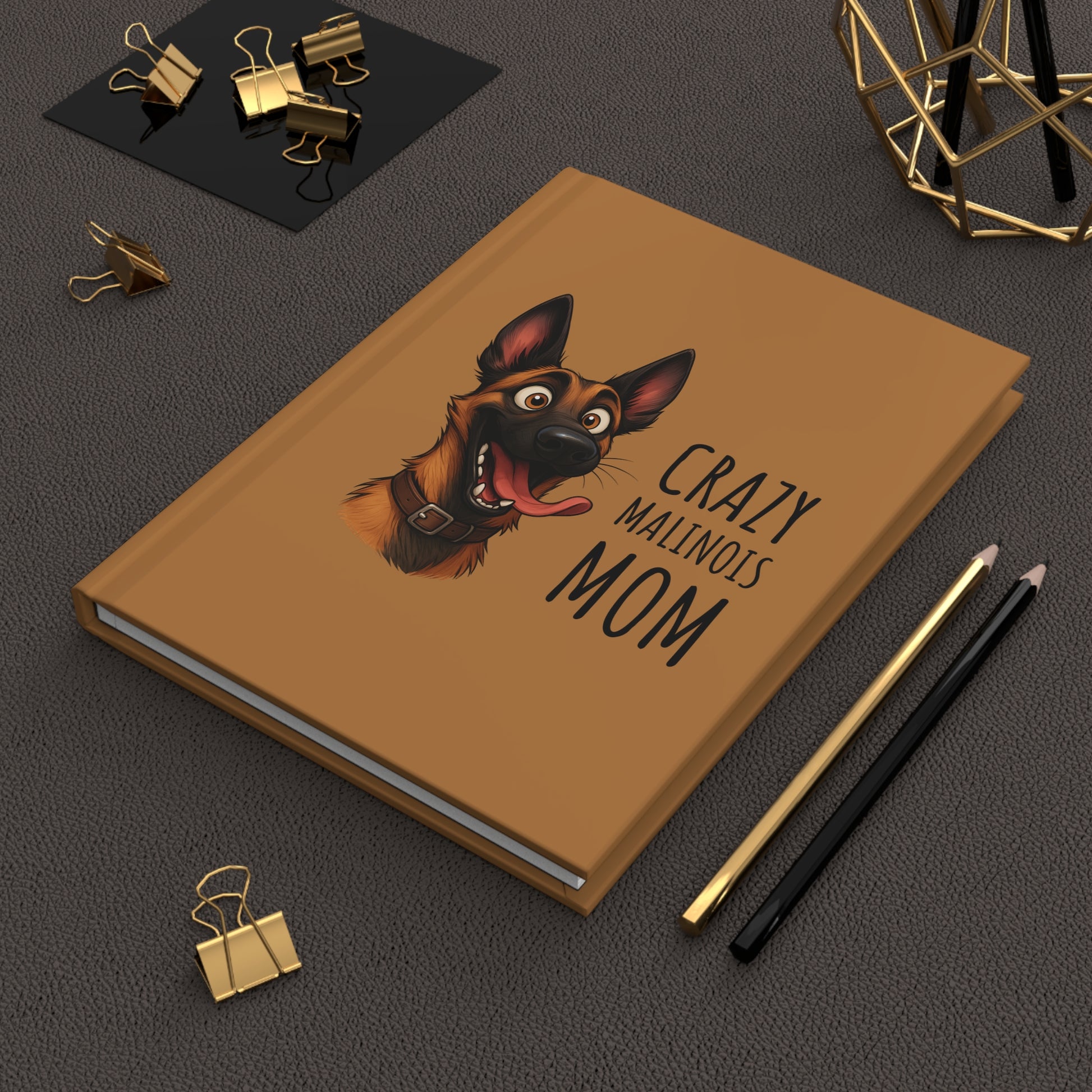 Brown notebook with a dog illustration and text on a dark surface with office supplies.